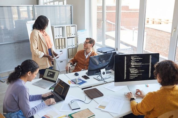 High angle view at multi-ethnic software development team using computers and writing code while collaborating on project in modern office, copy space