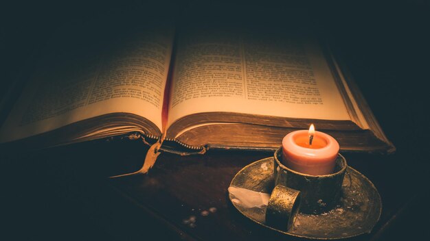 High angle view of lit candle and bible on table in darkroom