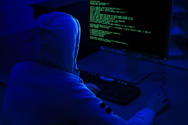 Hooded Figure Working on Computer in a Dark Room