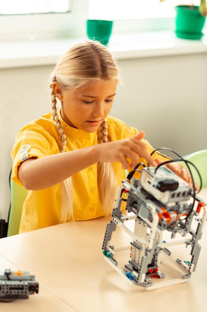 Koncentreret pige sidder ved sin naturvidenskabelige lektion og laver og tænder robot ved hjælp af byggesæt.
