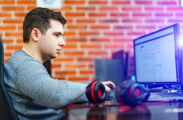 Koncentreret ung mand sidder på kontoret og arbejder på en stationær pc. Forretningsmand ser på computerskærmen, mens han udvikler nye teknologier i IT-virksomheden