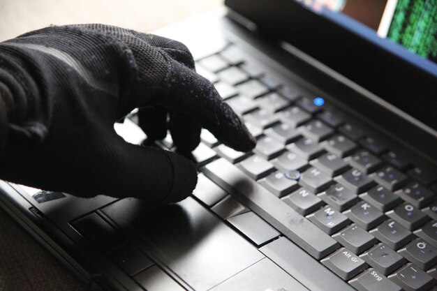 Konceptuelt billede af person med handsker, der bruger en computer med cybersikkerhed og trussel om at blive hacket