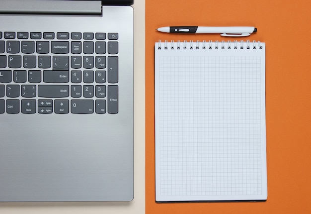 Laptop, notesbog med pen på brunt papir. Studio skud