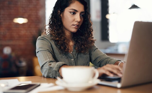 Laptop typing and woman in cafe for remote work research and online planning with business notes Thinking ideas and freelance consultant in coffee shop with computer drink or writing web article