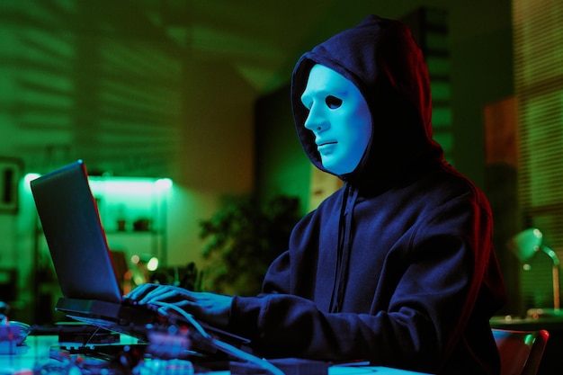 low angle shot of anonymous with white mask doing web crime
