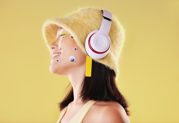 makeup music headphones and woman in studio isolated on a yellow background eye stickers technology and smile of happy female model listening enjoying and streaming radio podcast and audio song