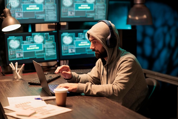 Man hacker breaking through security system and hacking computer server, working at night. Dangerous criminal with hood stealing hardware information and big data, using virus to hack.