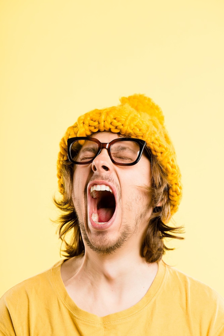 Foto man tired and yawn with winter hat fashion and sleepy with funky beanie style in studio nerd yell face and glasses with hipster rest and cool accessory with yellow background break and mockup