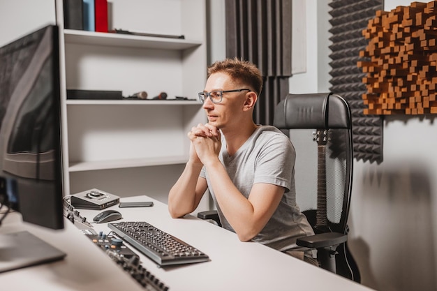 man working in music studio using computer wearing glasses sound engineer working and mixing track programmer watching at display of it while listening music technology concept