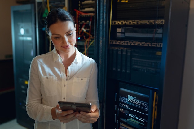 midadult woman using tablet while checking network cables in server room with blinking leds