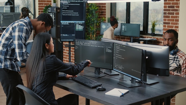 Mixed team of programmers analyzing source code pointing at screens comparing algorithm with user interface on digital tablet. Software developers working on cyber security group project.