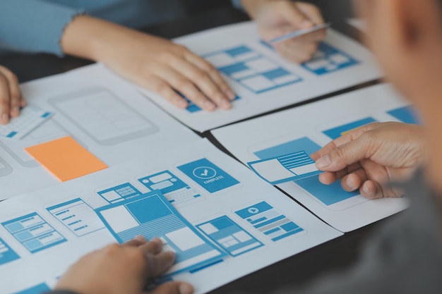 Närbild ux-utvecklare och ui-designer brainstormar om mobilappgränssnittets trådramdesign på bordet med kundkort och färgkod på ett modernt kontor. Kreativ digital utvecklingsbyrå