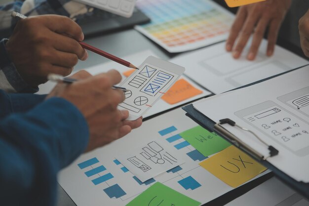 Närbild ux-utvecklare och ui-designer brainstormar om mobilappgränssnittets trådramdesign på bordet med kundkort och färgkod på ett modernt kontor. Kreativ digital utvecklingsbyrå