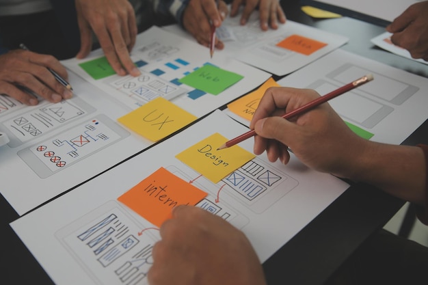 Närbild ux-utvecklare och ui-designer brainstormar om mobilappgränssnittets trådramdesign på bordet med kundkort och färgkod på ett modernt kontor. Kreativ digital utvecklingsbyrå
