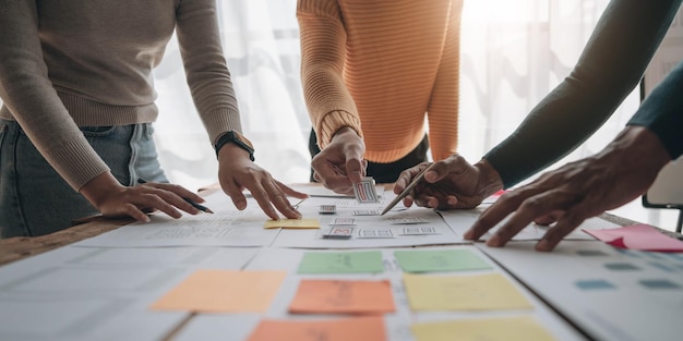 Närbild ux-utvecklare och ui-designer brainstormar om mobilappgränssnittets trådramdesign på bordet med kundkort och färgkod på ett modernt kontor. Kreativ digital utvecklingsbyrå