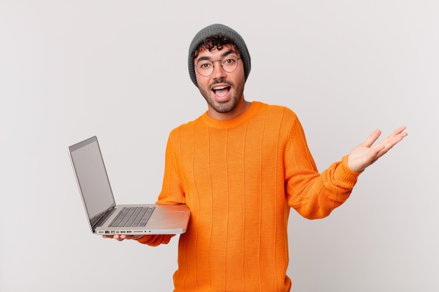 Nerd man with computer feeling happy, excited, surprised or shocked, smiling and astonished at something unbelievable