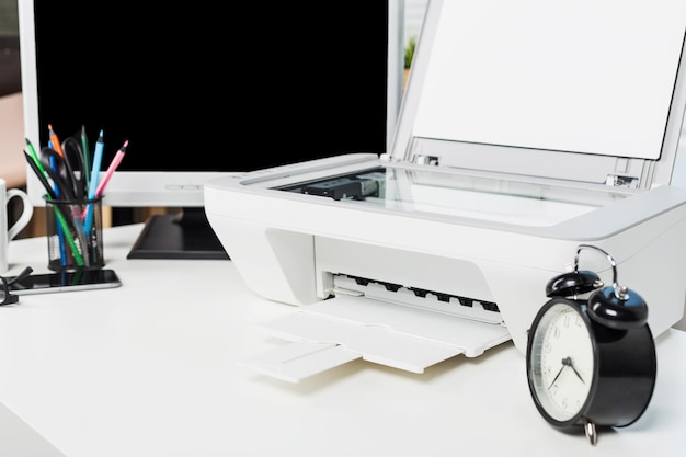 office workspace featuring a printer clock and stationery arranged on a desk with a blank monitor in the background