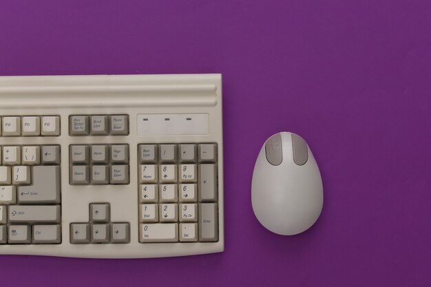 Old keyboard and pc mouse on purple background. Top view. Flat lay