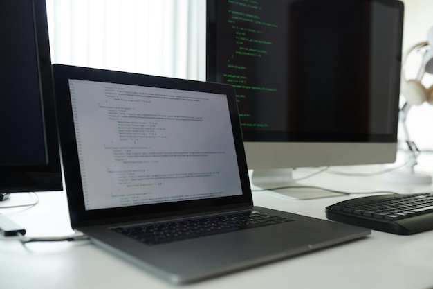 Opened laptop with programming code on desk of software developer