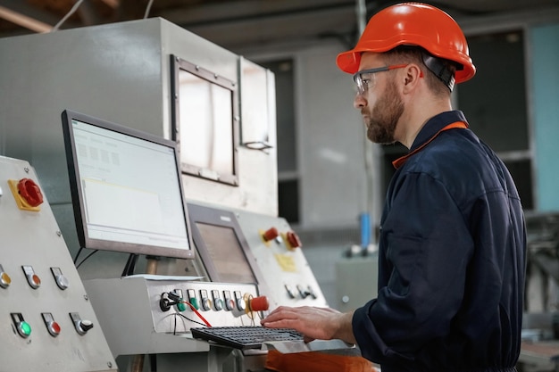Operating the machine Factory worker is indoors with hard hat
