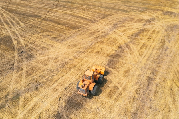 Orange tractor driving through the mown wheat field farmers at work agriculture harvesting season