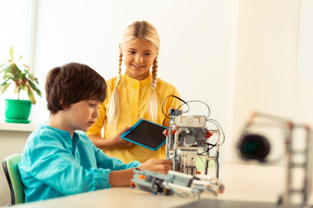 Pige står nær sin klassekammerat, der bygger en robot.