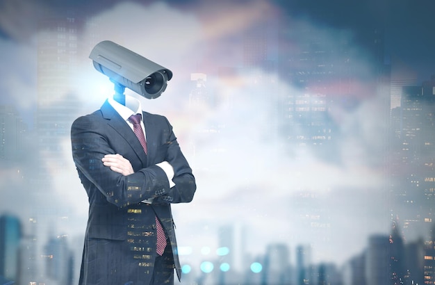 portrait of a businessman wearing a suit and standing with crossed arms. his head is a cctv camera. a cloudy sky cityscape background. toned image double exposure mock up