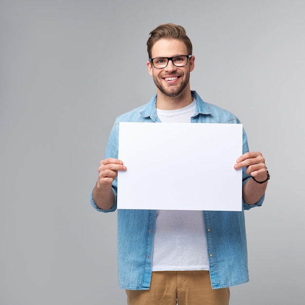 Portrait of a happy handsome young man holding blank white card or sign
