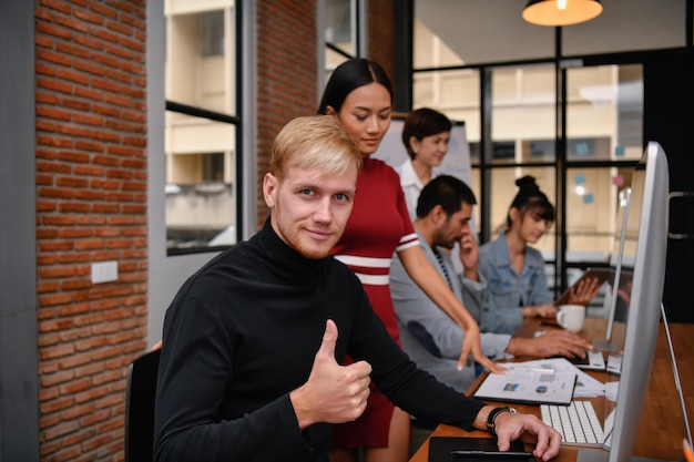 Portrait of businessman showing thumbs up while colleagues working in office