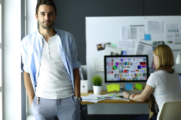 Portrait of young designer in front of laptop and computer while working Assistant using her mobile at background