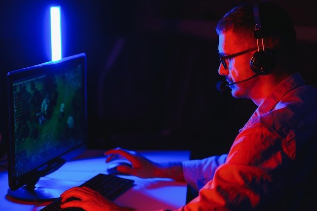 Professional Gamer Plays Video Game on His Computer. He's Participating in Online Cyber Games Tournament or in Internet Cafe. He Wears Glasses and Talks into Microphone.