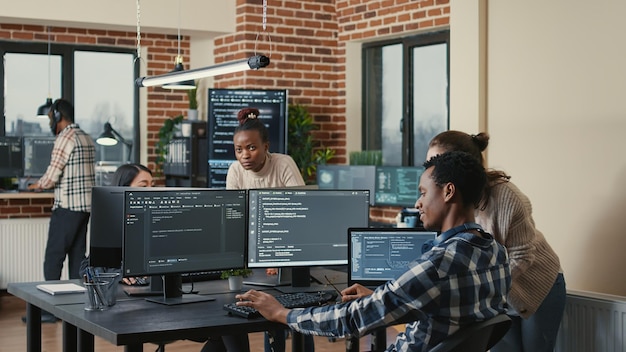 Programmer analyzing compiling code on multiple screens takes off glasses and doing high five hand gesture with colleague developer. Software developers celebrating successful coding.