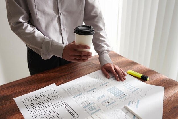 Project manager drinking cup of coffee when checking mobile app templates created by ui and ux desig