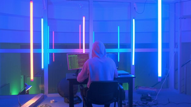 Rear view of man using computer in illuminated room