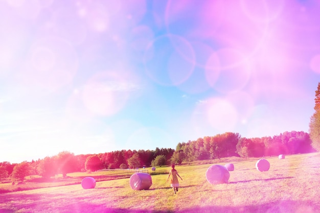 rear view of woman walking amidst hay bales on field