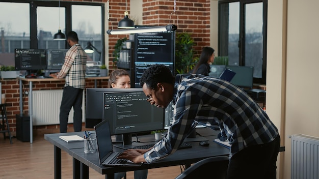 Senior developer coding on laptop at desk with computer screens parsing code in software agency. Programer compiling programming language with team innovating machine learning algorithms .