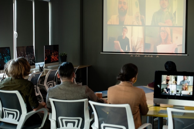 Several young speakers answering questions of audience sitting by desk in front of whiteboard in auditorium during video conference