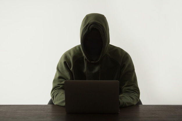 silhouette of a man in a hood sitting at a table with a laptop
