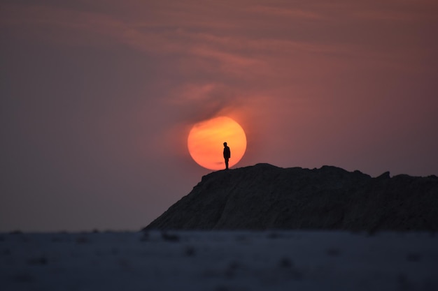 silhouette person on rock against sky during sunset