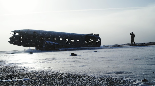 Silhouette person standing by abandoned airplane on sea shore against sky