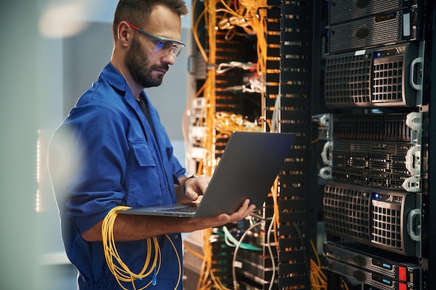 Silver colored laptop in hands Young man is working with internet equipment and wires in server room