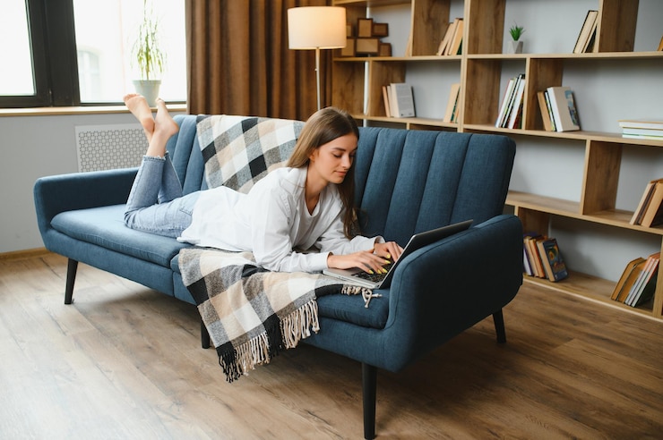 Foto smiling attractive young woman sitting on sofa using laptop communicating working online at home happy teen girl typing on computer enjoying writing blog or chatting with friends in social network