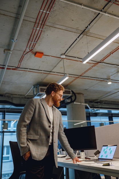 Smiling entrepreneur working with documents standing near desk in modern office