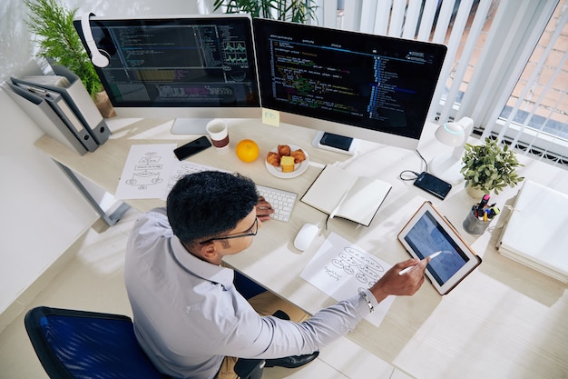 Software developer checking calendar on tablet computer when planning work on programming code for big project