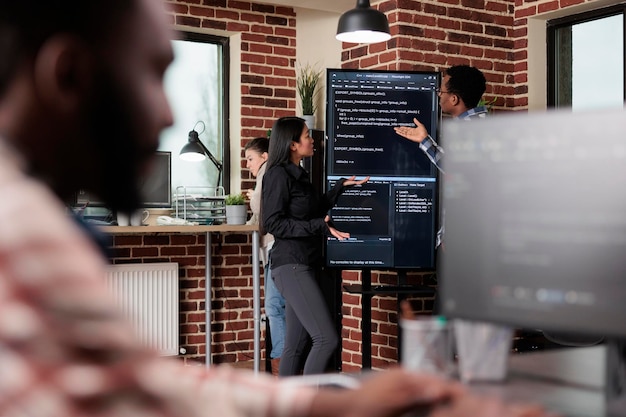 Software developers standing near vertical screen talking about interface bug and slow rate of processing data. Cybernetics engineers reviewing lines of code in order to secure mainframe database.