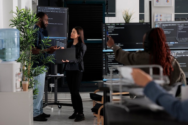 Softwareingeniører diskuterer algoritmer på storskærm og bærbar computer og analyserer HTML-scriptsprog. Team af systemprogrammører diskuterer database i terminalvindue, servergrænseflade.