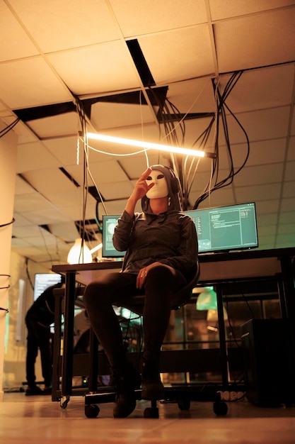 Spy with anonymous mask analyzing hologram to break into system, stealing passwords and sensitive data. Masked hacker using holographic image to cause computer malware, cyberterrorism.