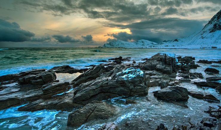 Bild strand vid norska havet på en stenig kust vid solnedgång på vintern