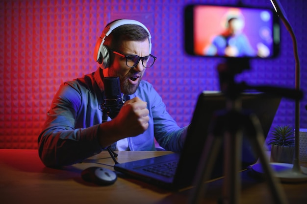 Streamer is streaming online contentmetaverse ar vrgaming and esports conceptHappy man gamer wear headphone competition video game online with Laptop computer in colorful neon lights