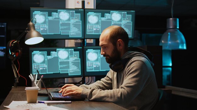 Stressed IT coder hacking security system on computer, using pc malware to steal big data from server. Working at night with multiple monitors to hack database, being irritated. Handheld shot.